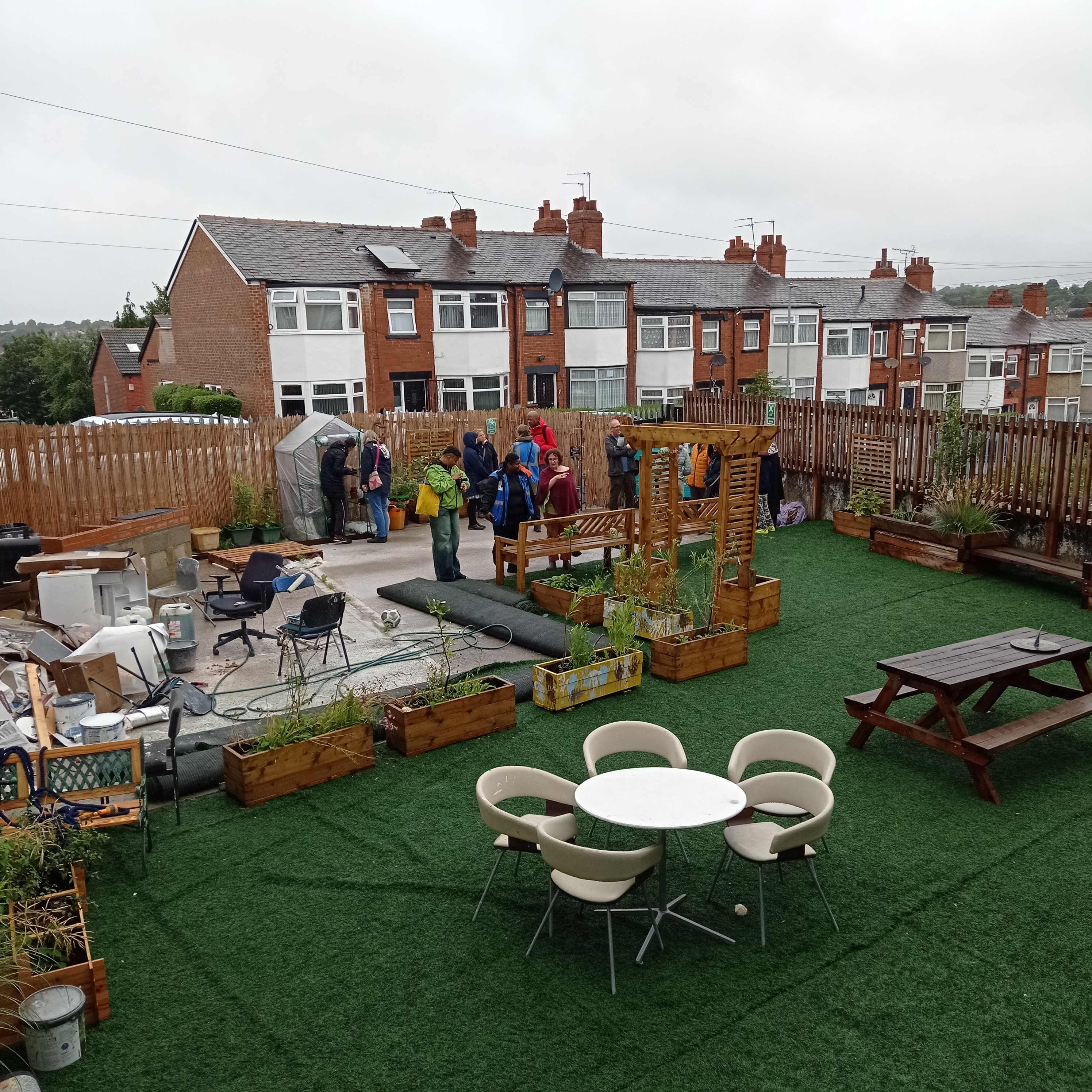 A cluster of people stand at the edge of a small back yard space behind an industrial building that is being turned into a community garden.